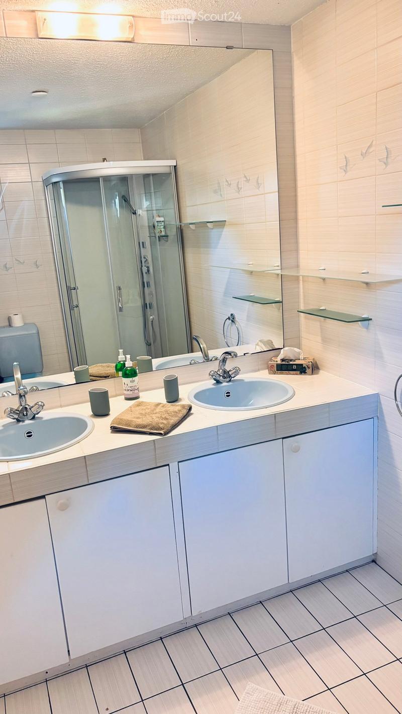 Modern bathroom with double sinks, large mirror, glass shower enclosure, white cabinets, and tiled floor.