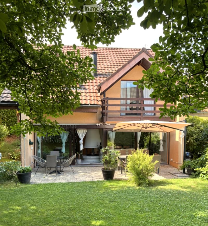 Garden area with a patio, outdoor furniture, umbrella, and a view of the house with a balcony and large windows.