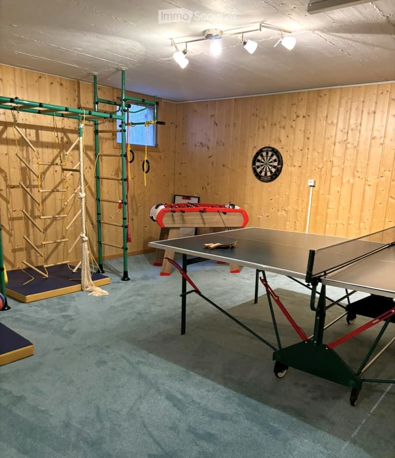 A recreational room with wooden walls, a ping pong table, a foosball table, a dartboard, and gymnastics equipment.