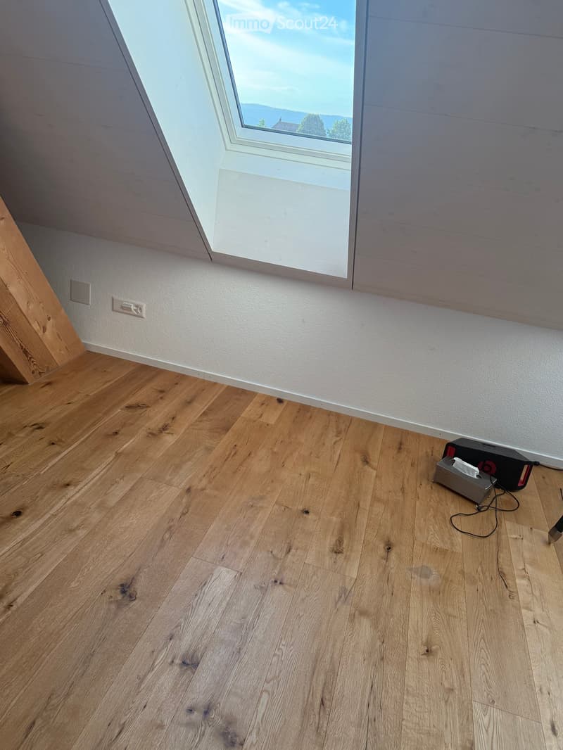Empty room with wooden flooring, white walls, and a skylight window offering a view of the outdoors.