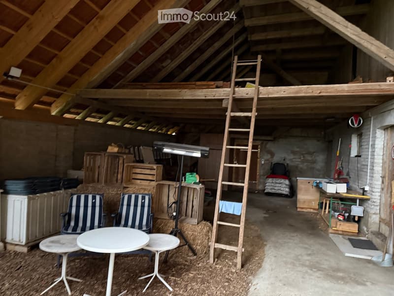 An attic space with exposed wooden beams, a ladder leading to a loft area, and various furniture including a table, chairs, and cabinets.