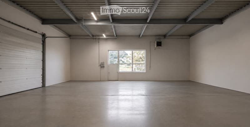 Empty garage with concrete floor, large garage door, small window, and overhead lighting.