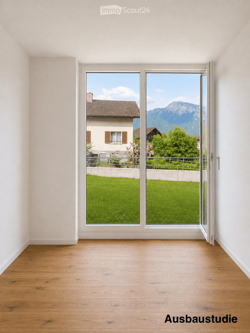 Empty room with wooden flooring and large windows offering a view of a green lawn, a house, and mountains in the background.