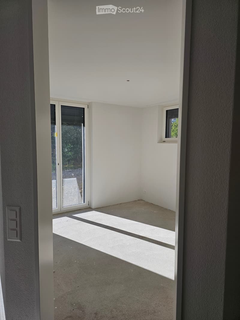 Empty room with white walls, grey carpeted floor, large sliding glass door, and small window. No furniture or equipment visible.