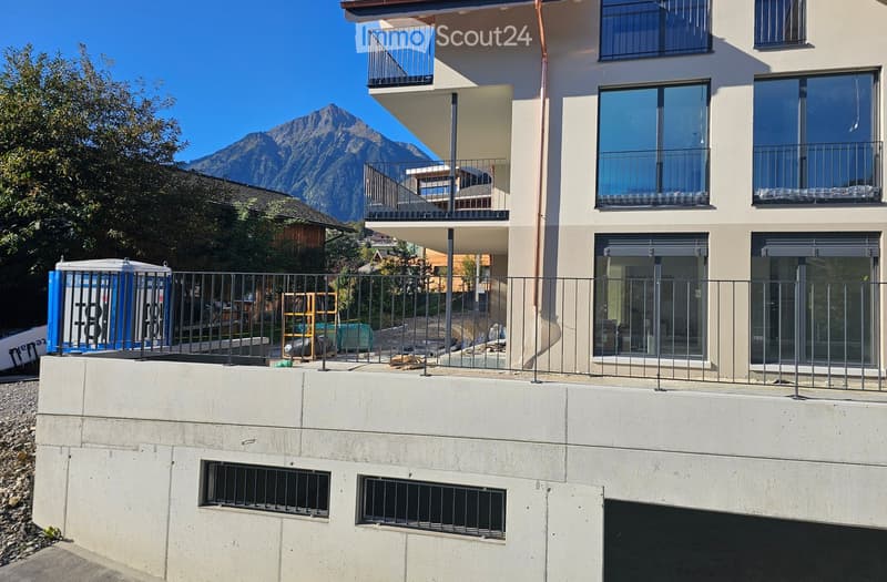 Modern multi-story building with balconies, large windows, and a scenic mountain view in the background.