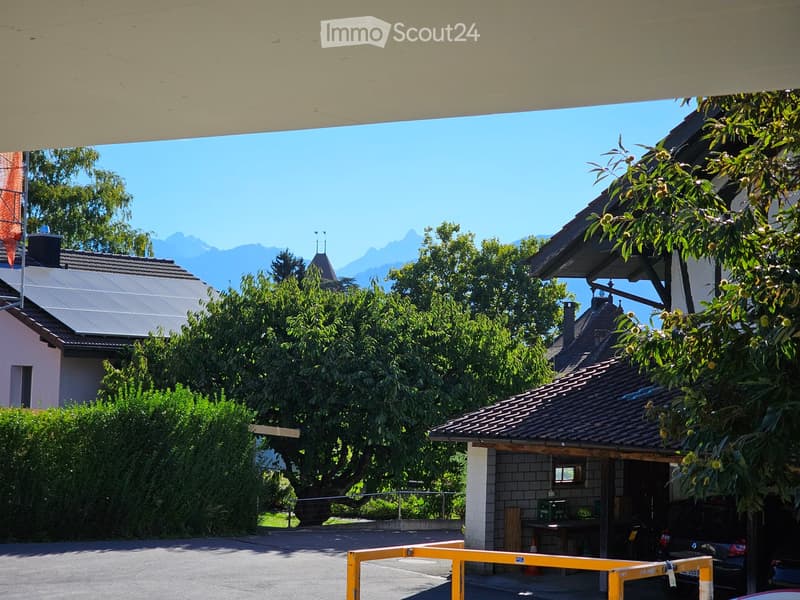 Residential building with a tiled roof, surrounded by trees and greenery, with a clear view of mountains in the background.
