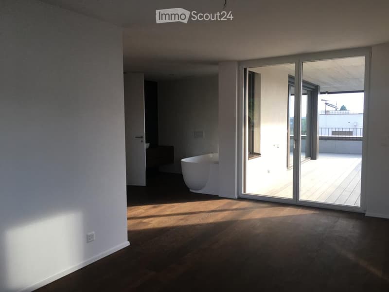 Empty room with wooden flooring, white walls, large sliding glass doors leading to a balcony, and a bathtub visible in the background.