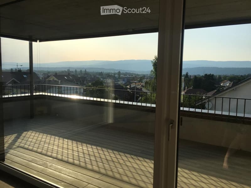 Modern balcony with wooden decking, glass railing, and scenic city and mountain view.