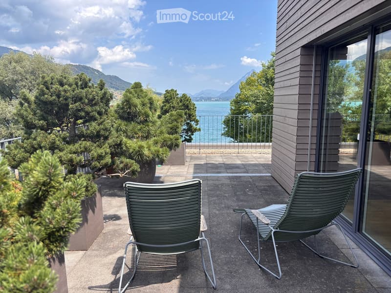 Balcony with two green lounge chairs, potted plants, and a scenic mountain and lake view.