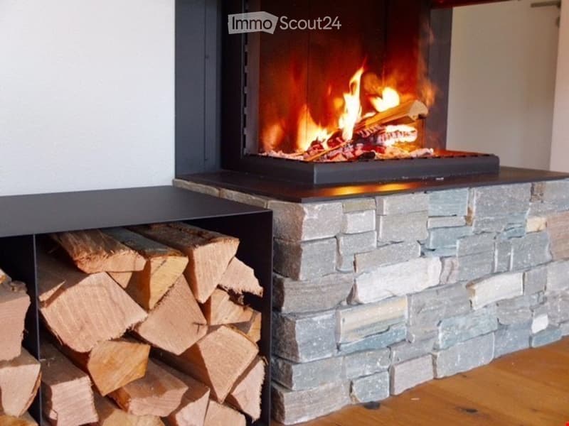 Modern living room with a stone fireplace and neatly stacked firewood beside it.