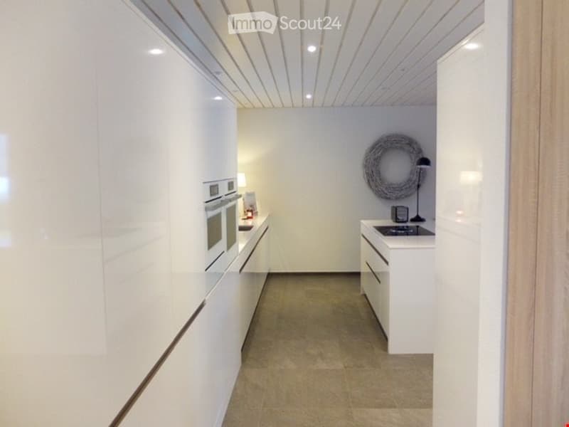 Modern, minimalist kitchen with white cabinetry, a built-in oven, a sink with a faucet, and a decorative wreath on the wall.