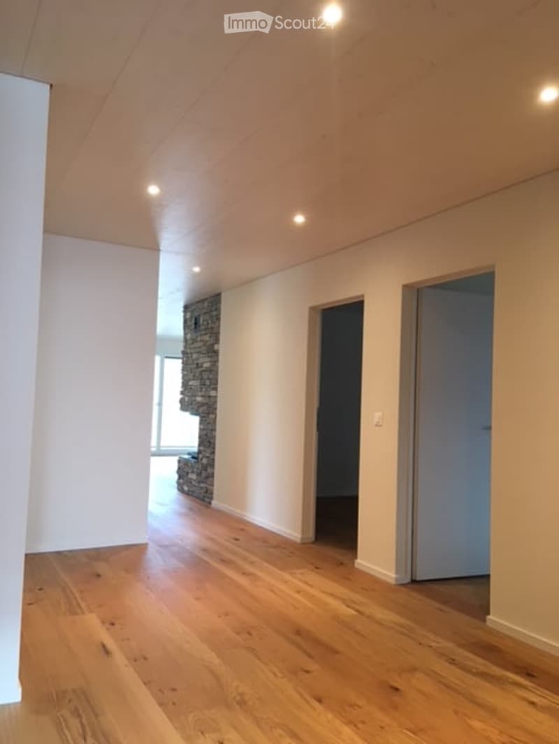 Empty room with wooden flooring, white walls, and recessed lighting. Features a stone accent wall and two doors leading to other spaces.