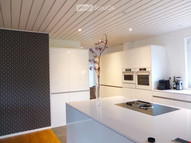 Modern kitchen with white cabinets, a central island with an induction cooktop, and built-in ovens. Features a sleek design with a decorative vase on the island.