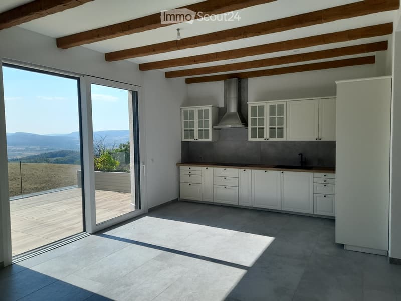 Modern kitchen with white cabinets, stainless steel range hood, and a large sliding glass door opening to a patio with scenic mountain views.