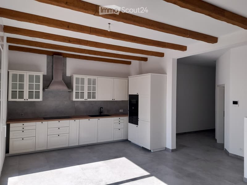 Modern kitchen with white cabinets, wooden countertops, stainless steel sink, and built-in oven. Exposed wooden beams on the ceiling.