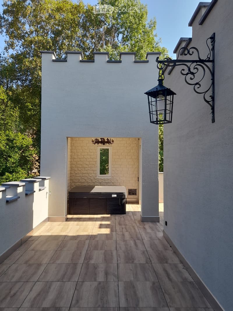 A modern outdoor patio with wooden tiles, a built-in hot tub, and decorative lanterns on the walls.