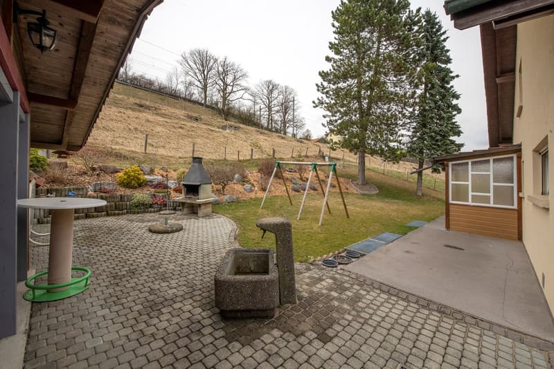 Garden area with a brick-paved patio, outdoor table, swing set, barbecue, and a small shed.