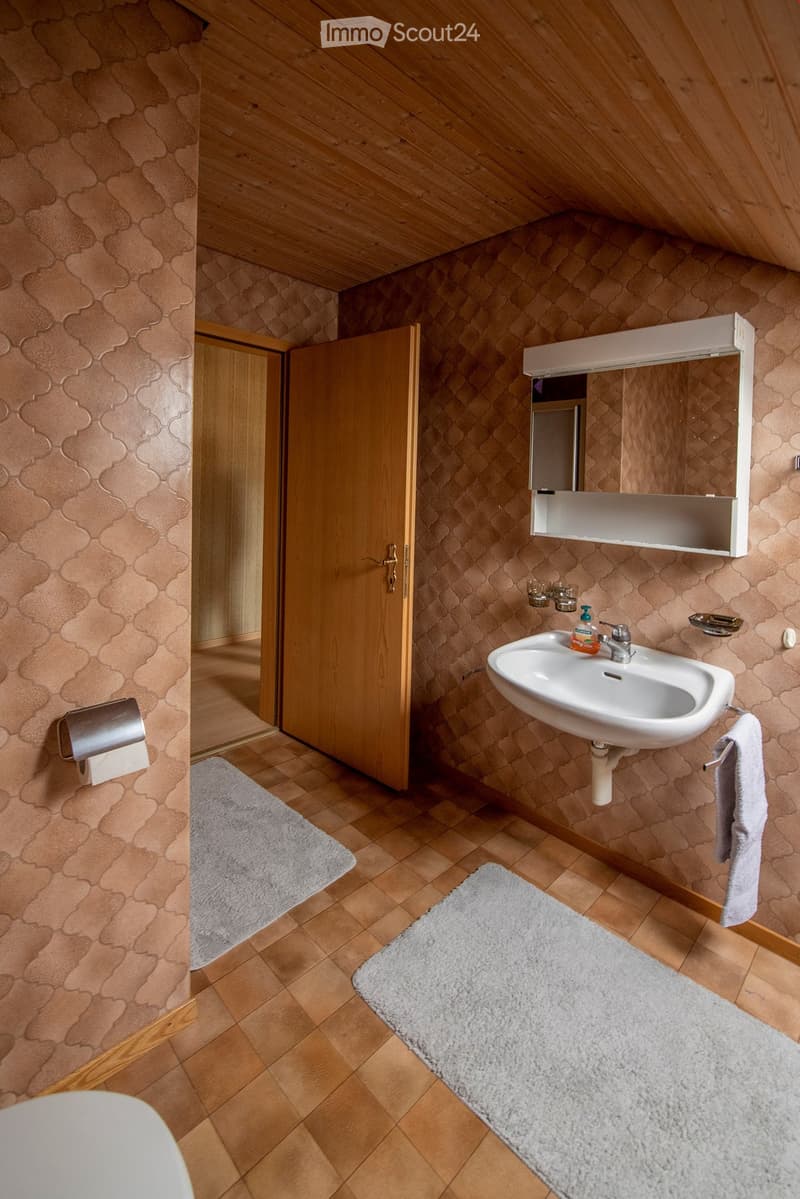 Bathroom with wooden floors, patterned walls, a sink with a mirror, a towel, and a toilet paper holder.