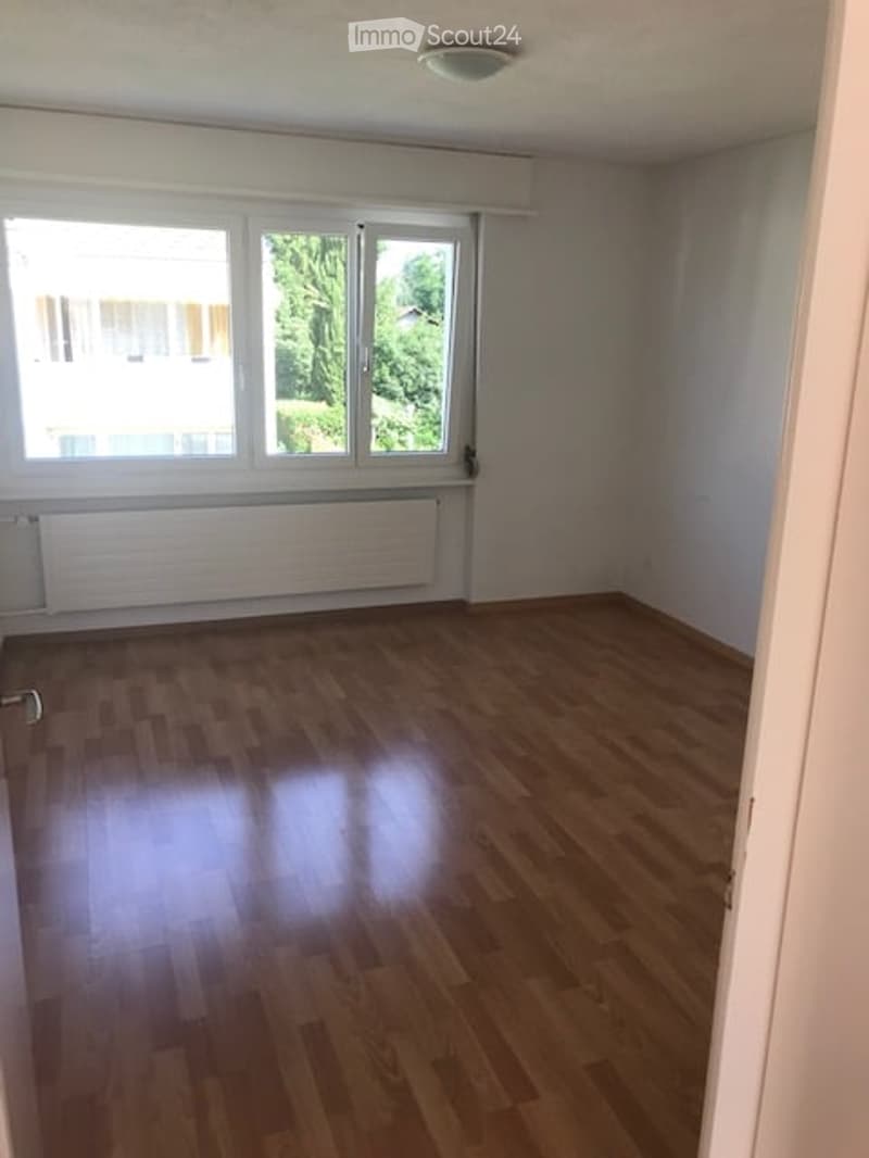 Empty room with wooden flooring, large windows, radiator, and white walls.