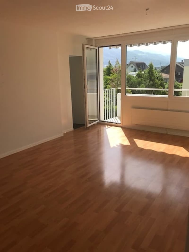 Empty room with wooden flooring, large windows, and a view of the mountains and trees outside.