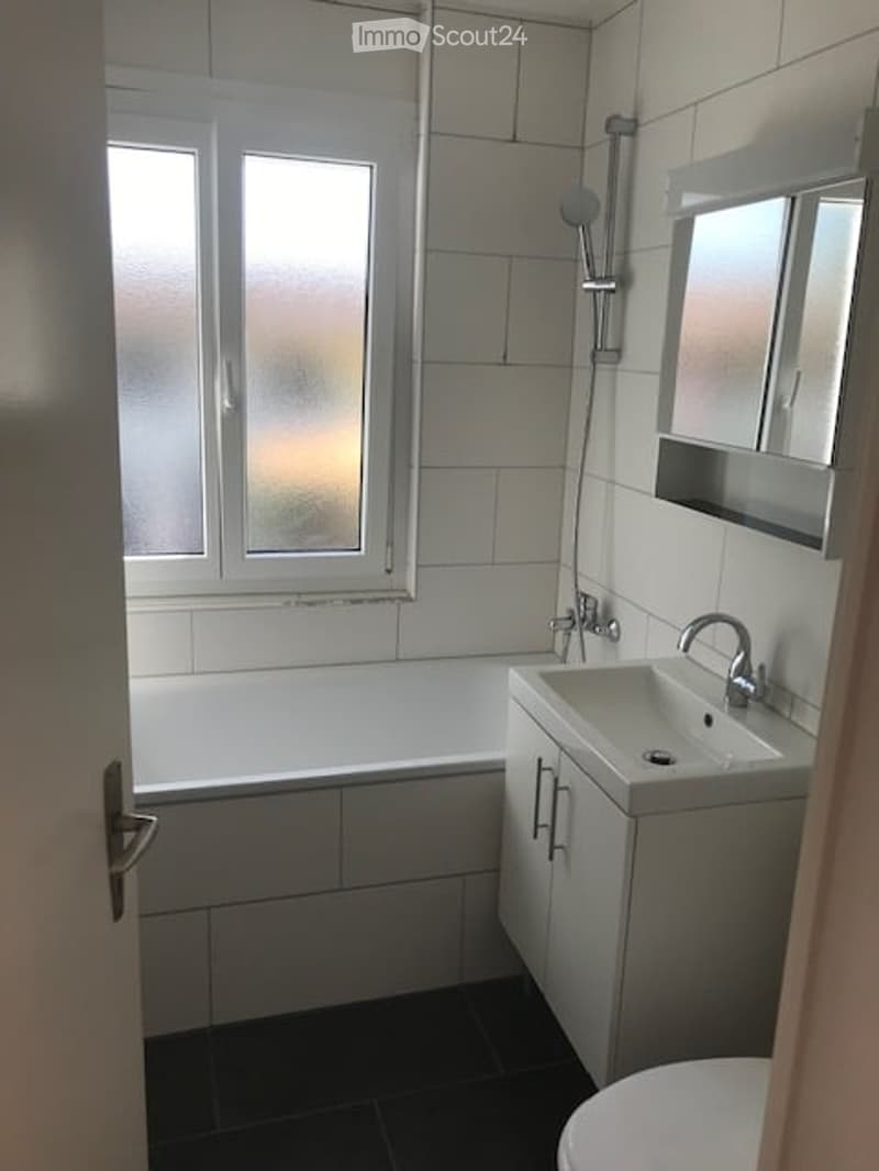 Modern bathroom with white tiles, a bathtub, a sink with a cabinet, a mirror, and a shower fixture.