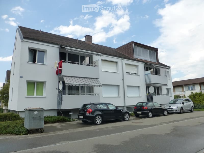 3 story house, white wall, grey roof, balcony, two cars parked on the street