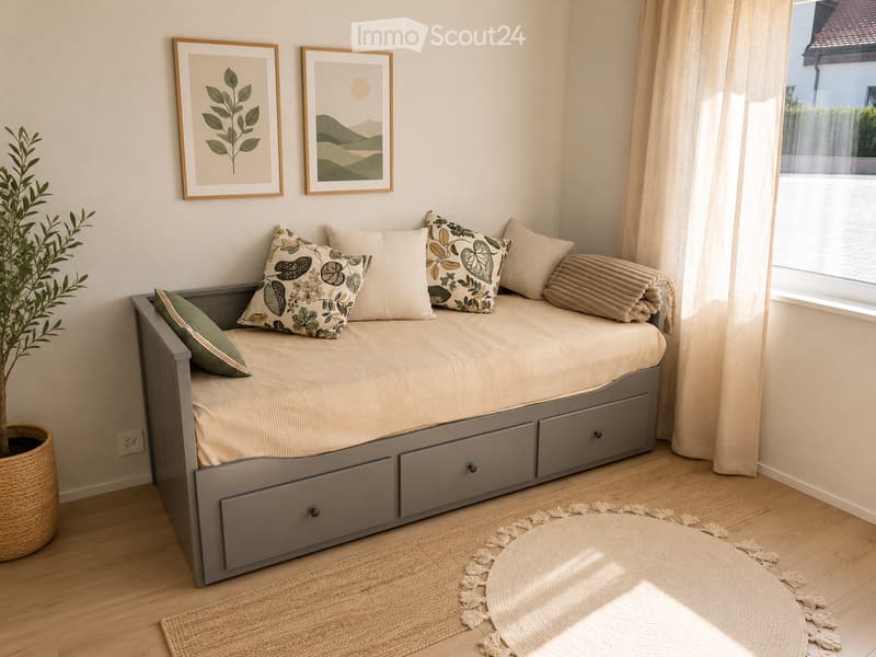 Cozy bedroom with a daybed, multiple pillows, storage drawers, a round woven rug, a potted plant, and framed artwork on the wall.