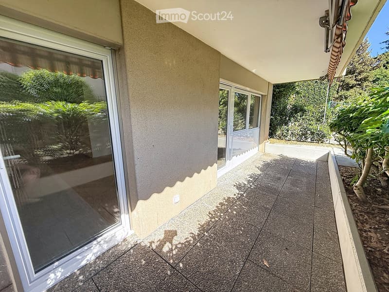 Balcony with tiled floor, large sliding glass door, view of greenery, and covered roof section.