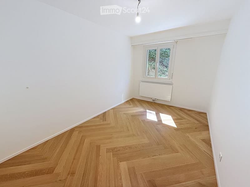 Empty room with wooden herringbone flooring, white walls, and a single window with white frame. No furniture or equipment present.