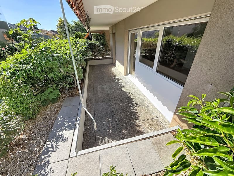 Balcony with tiled flooring, large glass sliding doors, and surrounding greenery.