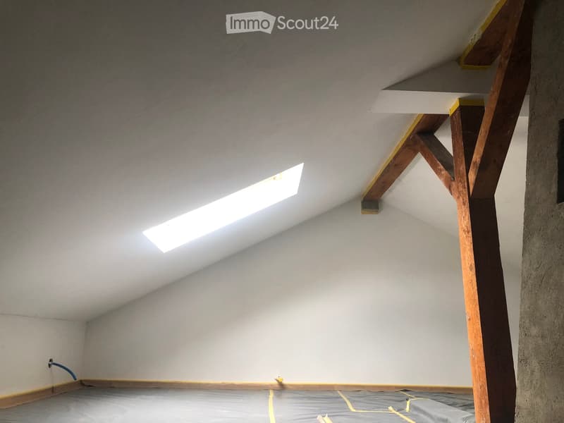 Empty attic space with exposed wooden beams, skylight window, and unfinished walls.