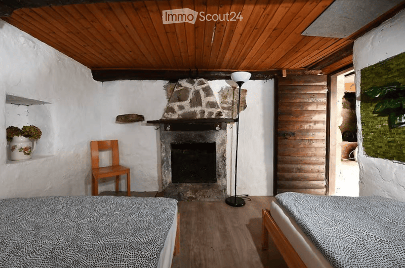Cozy bedroom with wooden floors, exposed wooden ceiling beams, fireplace, two single beds, a wooden chair, and a floor lamp.