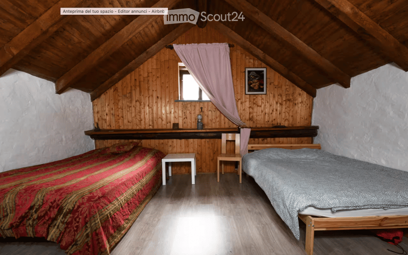 Cozy attic bedroom with wooden walls and slanted ceilings, featuring two single beds, a small table, and a chair.