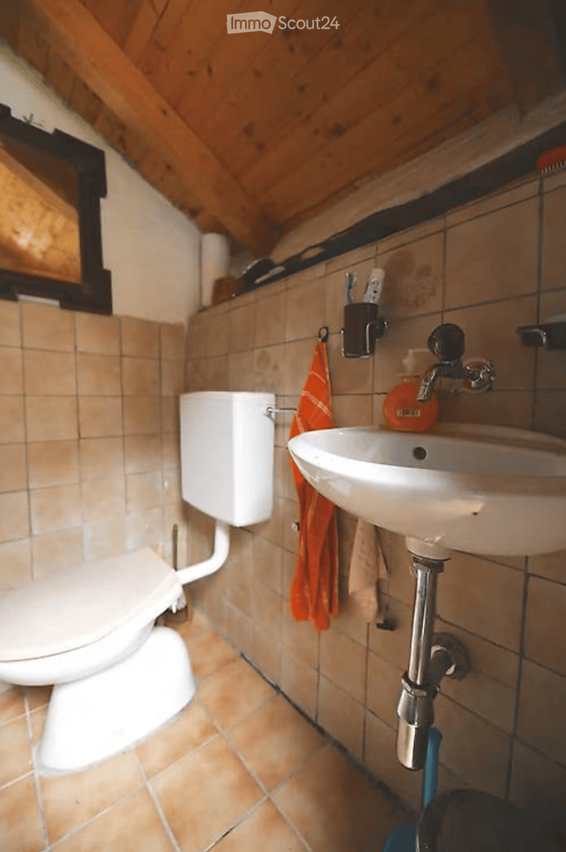 Bathroom with tiled walls and floor, a toilet, a sink with a faucet, a toothbrush holder, and an orange towel hanging on the wall.