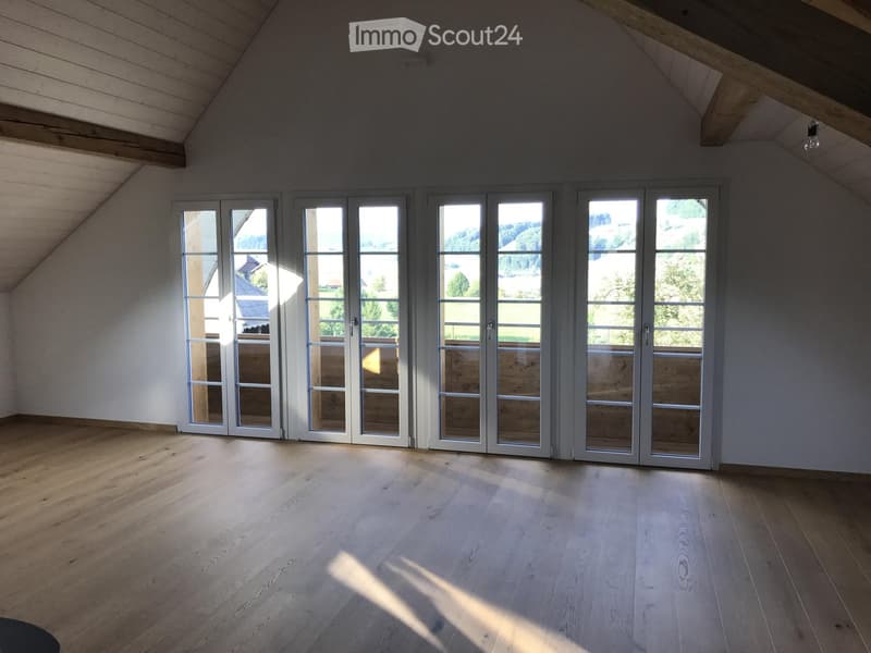 Empty attic room with wooden flooring, large windows, and exposed wooden beams on the ceiling.