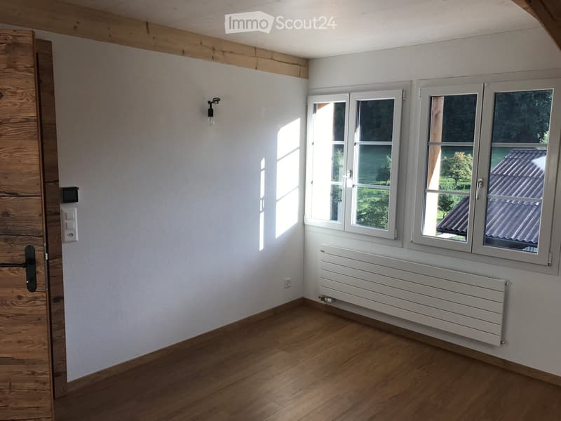 Empty room with wooden flooring, white walls, large windows, and a radiator. No furniture or equipment present.