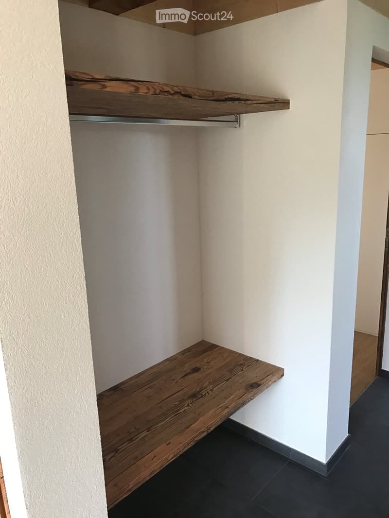 Corner shelf with wooden plank and metal support, white walls, dark tiled floor.