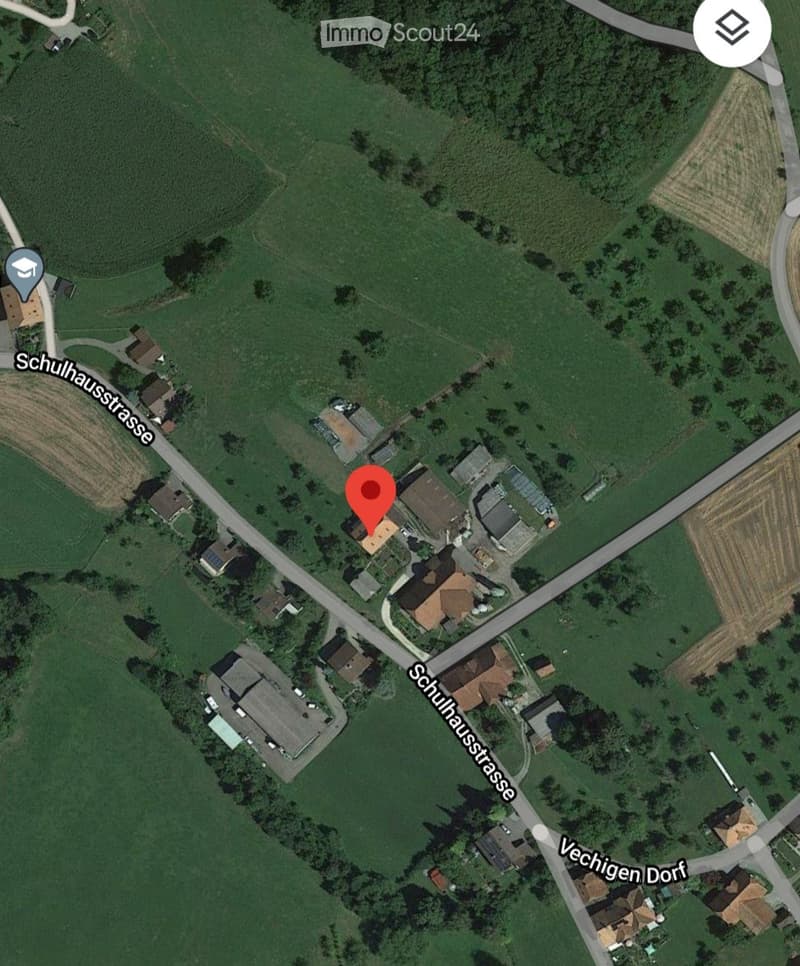Aerial view of a rural residential area with multiple houses, surrounded by green fields and agricultural land. The area includes a road named Schulhausstrasse and a nearby village named Vechigen Dorf.