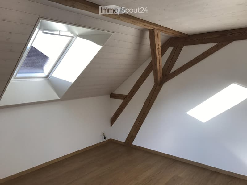 Empty attic space with wooden beams, white walls, and skylights allowing natural light to enter.