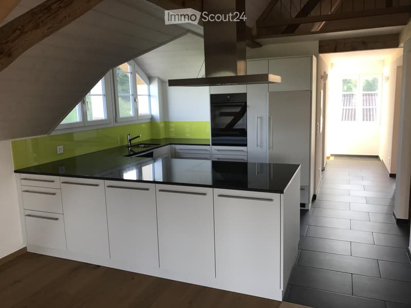 Modern kitchen with white cabinets, black countertops, stainless steel appliances, and a green backsplash. Features an island with a sink and faucet, and a built-in oven with a range hood.