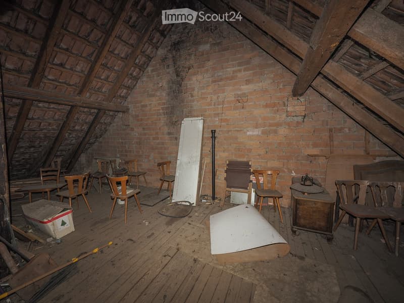 An attic space with exposed wooden beams and brick walls, furnished with several wooden chairs, tables, and a cabinet.