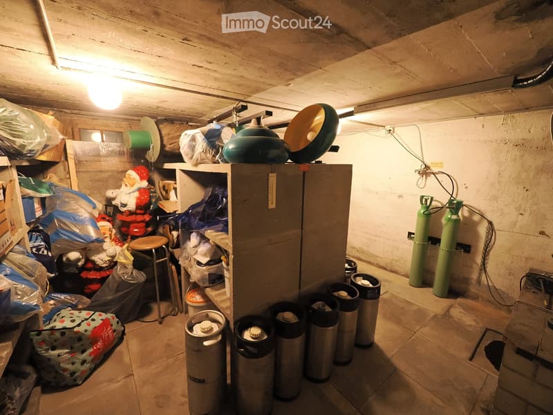 Storage room with exposed wooden ceiling, shelves, barrels, gas cylinders, and a small stool.