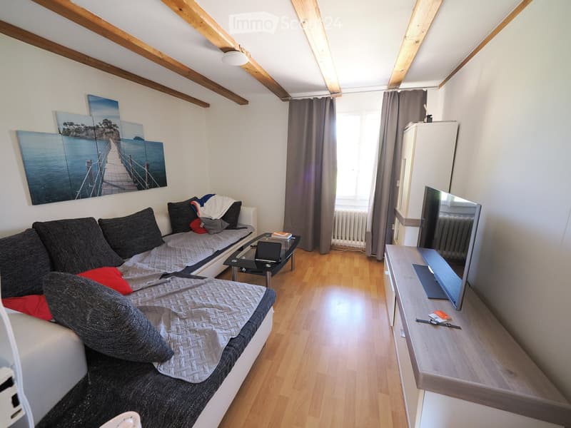 A cozy living room with a sofa, a small table, a TV, and a painting on the wall.