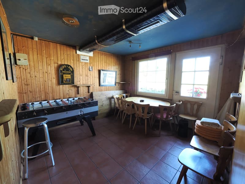 A cozy room with wooden walls, a foosball table, a round table with chairs, and a stool near the foosball table.