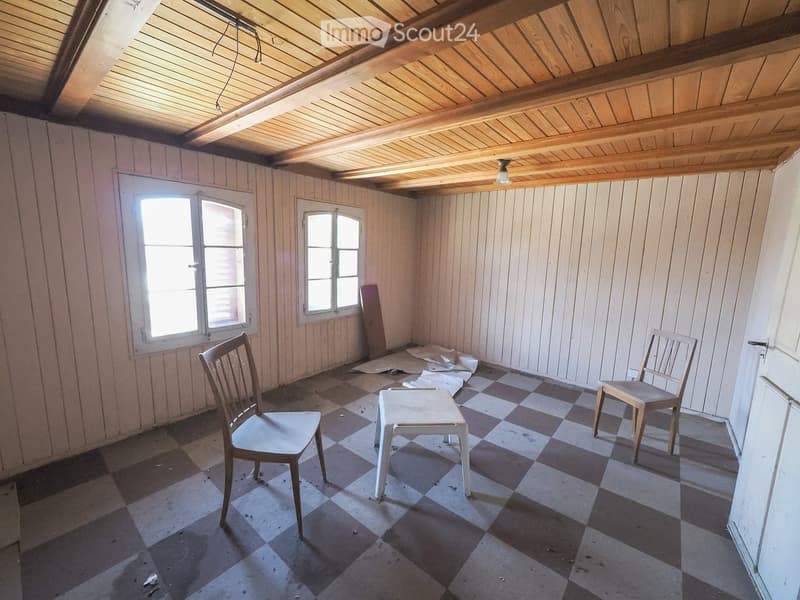 An unfurnished attic room with wooden walls and ceiling, checkered floor, two chairs, and a small stool.