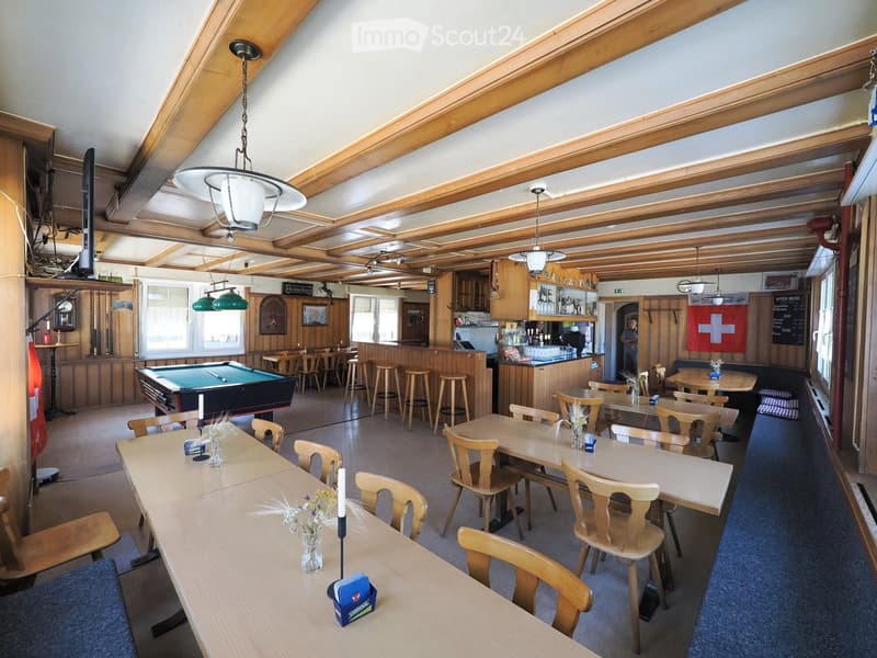 Restaurant or bar area with wooden tables, chairs, stools, a pool table, and a bar counter. Wooden beams on the ceiling and large windows.