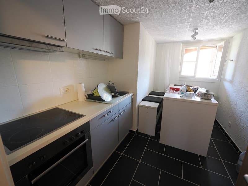 Modern kitchen with white cabinets, black tiled floor, induction cooktop, oven, sink, and small seating area with stools.