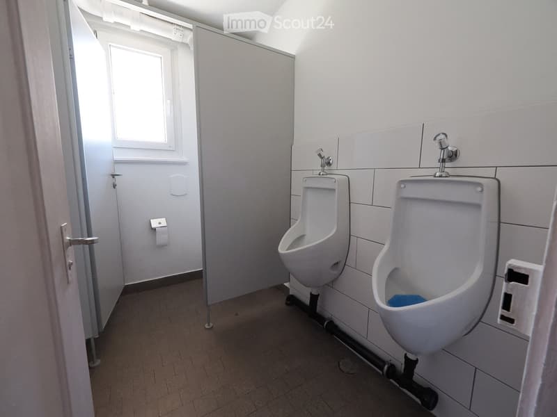 Modern bathroom with two urinals mounted on tiled walls, a window, and a door with a handle.