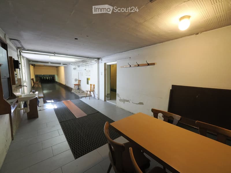 A small, furnished room with a table, chairs, and a sink. The room has tiled floors and walls, with a doorway leading to another area.