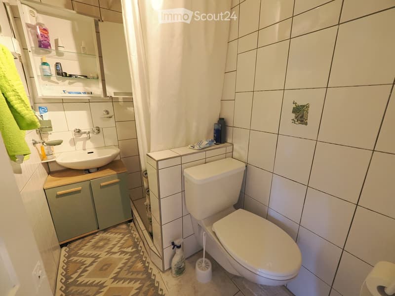 Modern bathroom with white tiles, a sink with a wooden cabinet, a toilet, a mirror, and a towel on the side.